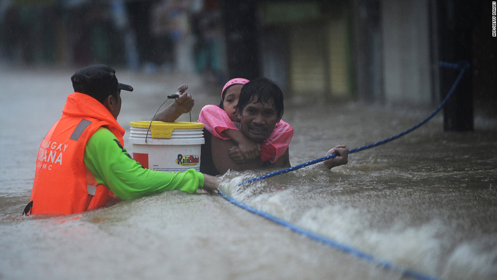 A rescuer guides a man carrying his daughter on his back through a strong current.