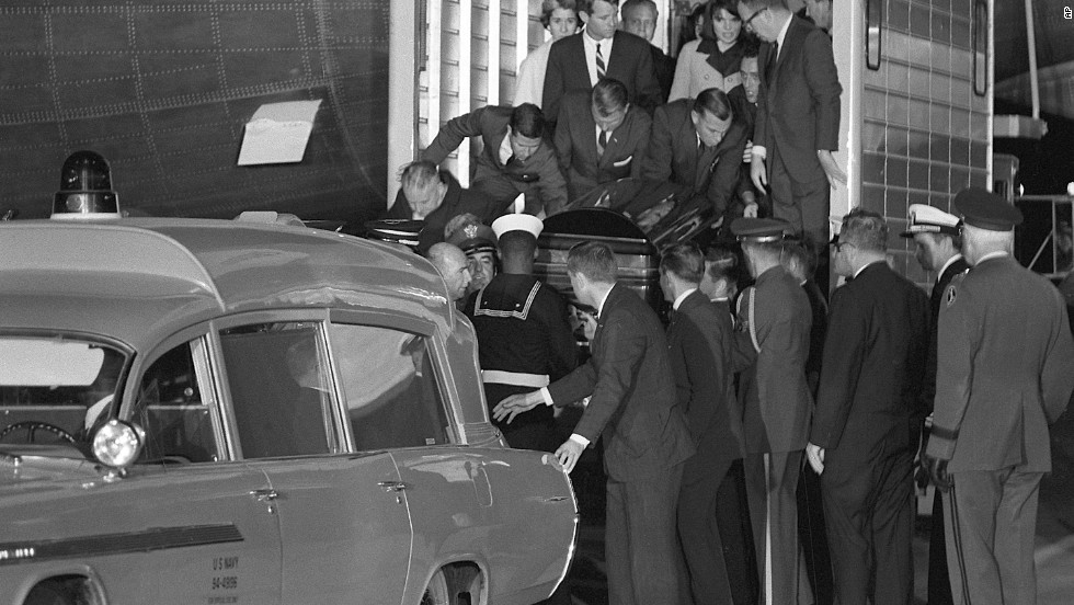 The casket containing the body of President Kennedy is moved to a Navy ambulance from the presidential plane. Jacqueline Kennedy and Attorney General Robert Kennedy stand behind on the elevator.