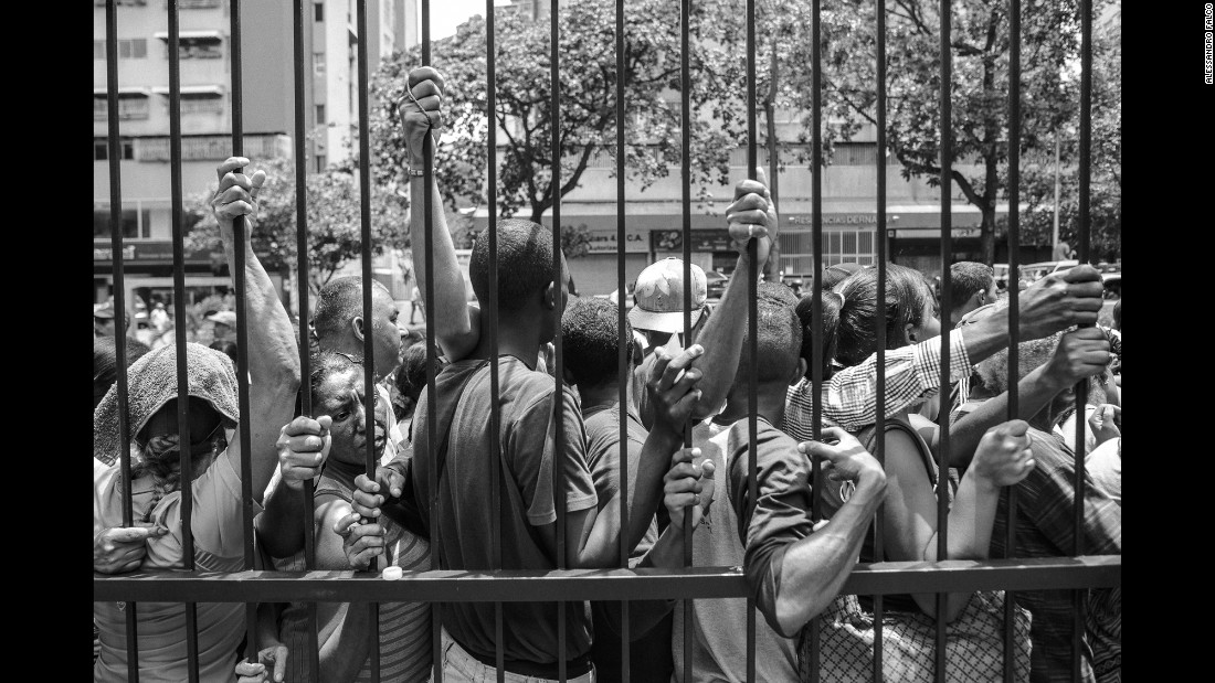 People line up in the hot sun to buy basic products in front of a supermarket in Caracas&#39; La Urbina district.