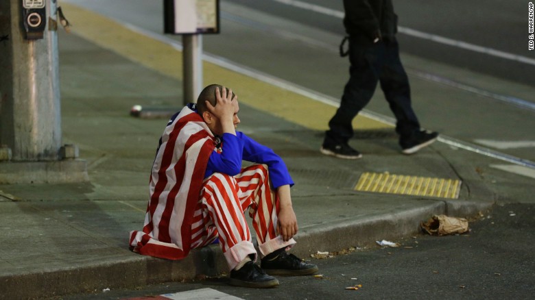 A man dressed in red, white and blue rests on a curb during a Trump protest Wednesday in Seattle.