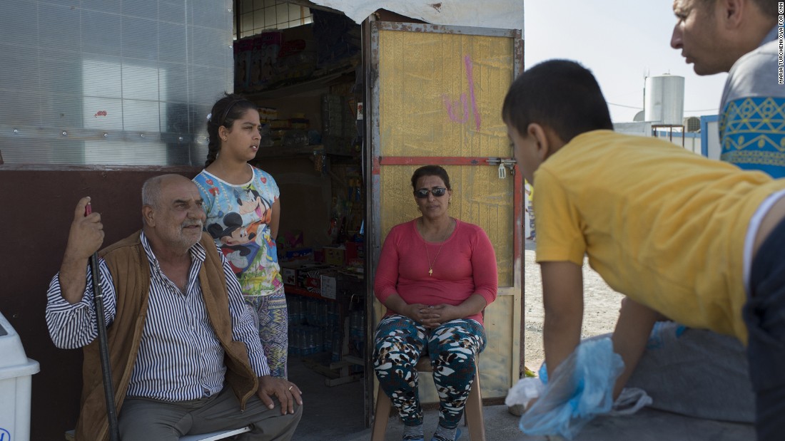 Raja Paulous, center, talks to neighbors at the entrance to her refugee camp grocery.