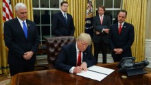 President Donald Trump, flanked by Vice President Mike Pence and Chief of Staff Reince Priebus, signs his first executive order on health care, Friday, January 20, in the Oval Office of the White House in Washington.