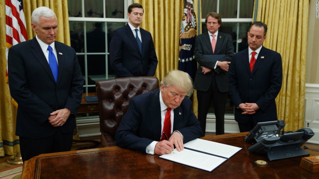 President Donald Trump, flanked by Vice President Mike Pence and Chief of Staff Reince Priebus, signs his first executive order on health care, Friday, January 20, in the Oval Office of the White House in Washington.