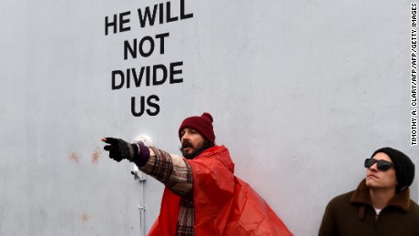 US actor Shia LaBeouf(L) during his He Will Not Divide Us livestream outside the Museum of the Moving Image in Astoria, in the Queens borough of New York January 24, 2017 as a protest against President Donald Trump.  
LaBeouf has installed a camera at the Museum of the Moving Image in New York that will run a continuous live stream for the duration of Trumps presidency. LaBeouf is inviting the public to participate in the project by saying the phrase, He will not divide us, into the camera. / AFP / TIMOTHY A. CLARY        (Photo credit should read TIMOTHY A. CLARY/AFP/Getty Images)
