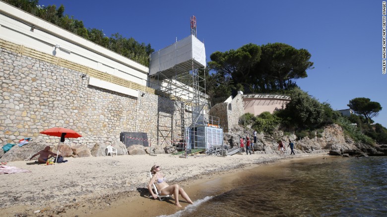 People sit and stand by the water as workers disassemble an elevator on the public beach near the Saudi King&#39;s villa in the Golfe-Juan seaside resort in Vallauris, southeastern France, on August 3, 2015. 