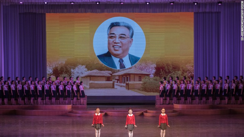Children stand before an image of late North Korean leader Kim Il Sung as they perform a variety dance and music show.