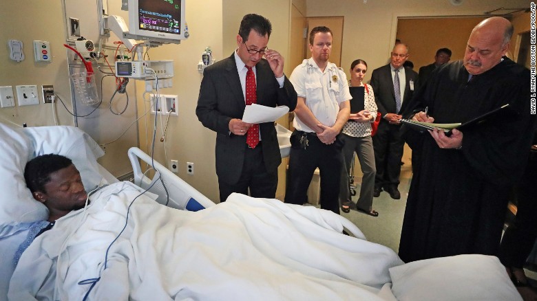 Bampumim Teixeira is arraigned from his hospital bed at Tufts Medical Center in Boston on Monday.
