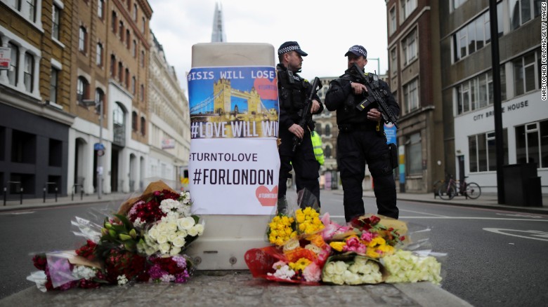 Armed police stand guard in front of floral tributes on Southwark Street near the scene of the attack. 