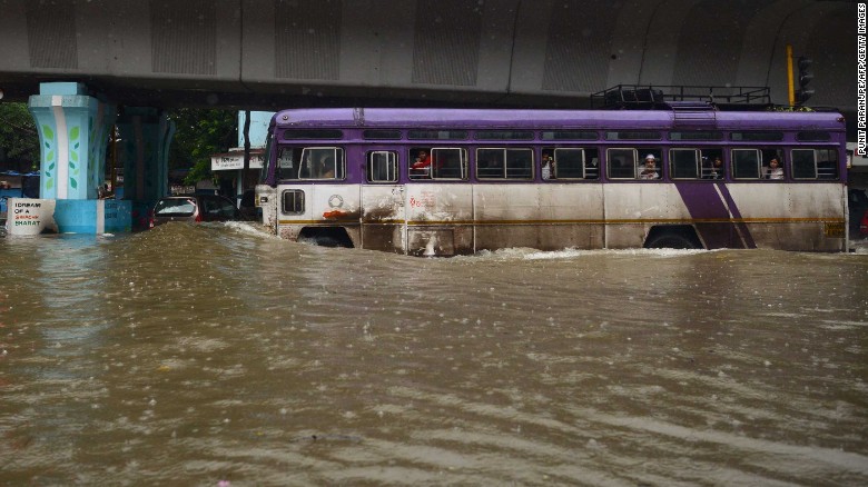 Residents are seen wading through a waterlogged street (above) while a bus tries to negotiatate another flooded road (below) in Mumbai on Tuesday. 