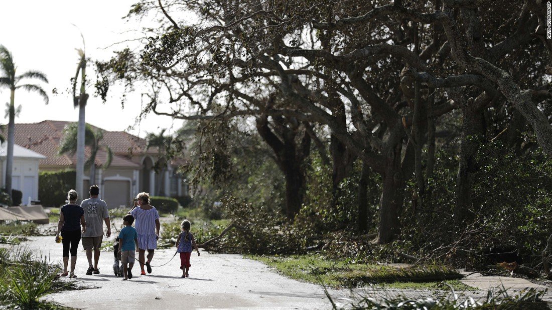 A family walks through a street littered with fallen branches from Hurricane Irma in Marco Island, Florida.