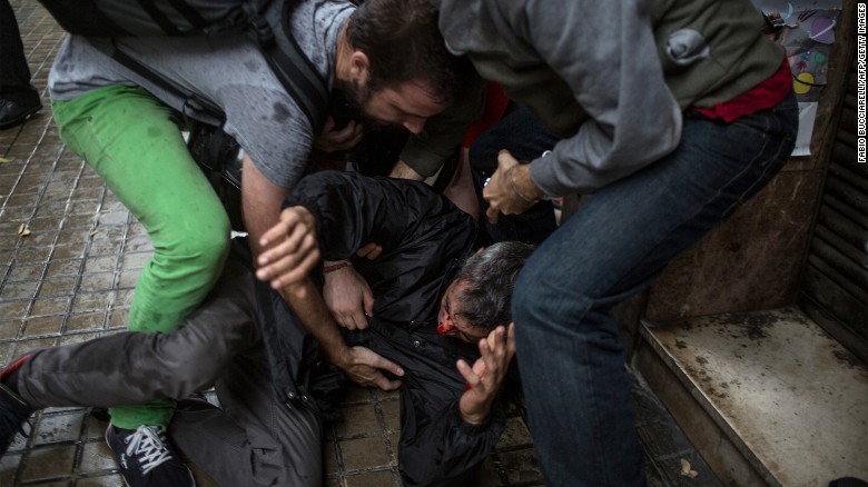 People help a man injured by a rubber bullet fired by Spanish police officers outside the Ramon Llull polling station in Barcelona.