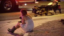 A woman sits on a curb at the scene of the shooting.