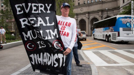 A Donald Trump supporter holds up an anti-Muslim poster as he awaits anti-Donald Trump protesters marching through the streets in Cleveland, Ohio,  near the Quicken Loans Arena site of the Republican National Convention July 18, 2016. / AFP / JIM WATSON        (Photo credit should read JIM WATSON/AFP/Getty Images)