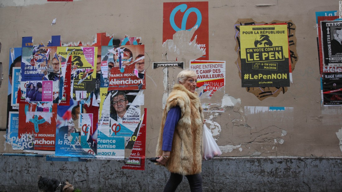 A woman walks past election campaign posters in Paris&#39; 18th district. One poster, in yellow, encourages voters to vote against Marine Le Pen. 