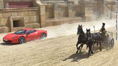 TOPSHOT - Ferrari driver Fabio Barone and his Ferrari 458 Italia competes against a Roman chariot drawn by two horses on &quot;Ben Hur&quot; movie set at Cinecitta World amusement park on May 11, 2017 in Castel Romano near Rome.  / AFP PHOTO / Andreas SOLARO        (Photo credit should read ANDREAS SOLARO/AFP/Getty Images)