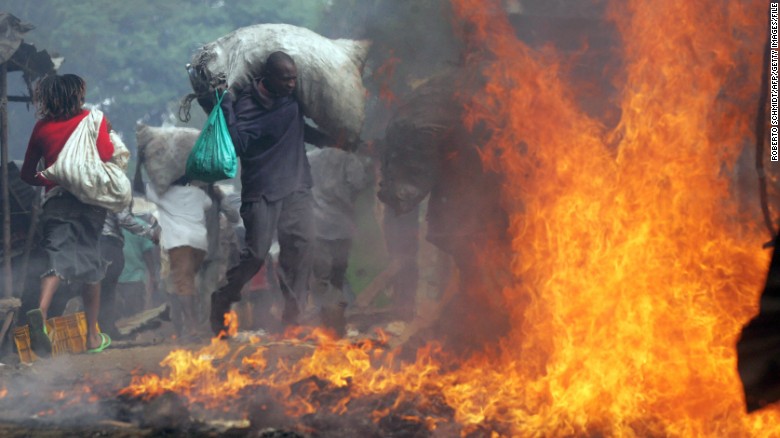 A resident of Kibera runs with a sack of charcoal he stole past a burning shack as he and thousands of other looters swept through the slum ransacking stores and setting cars and other property on fire 31 December 2007. 